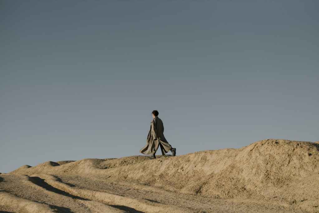 man in black jacket walking on brown sand