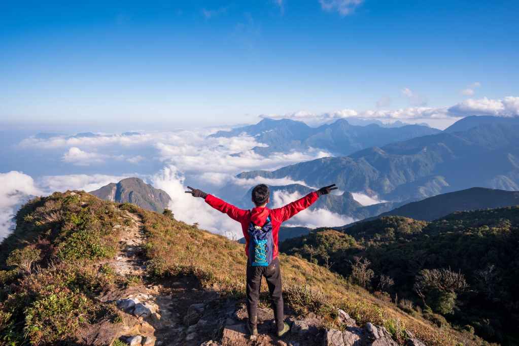 photo of man standing on mountain while doing peace sign