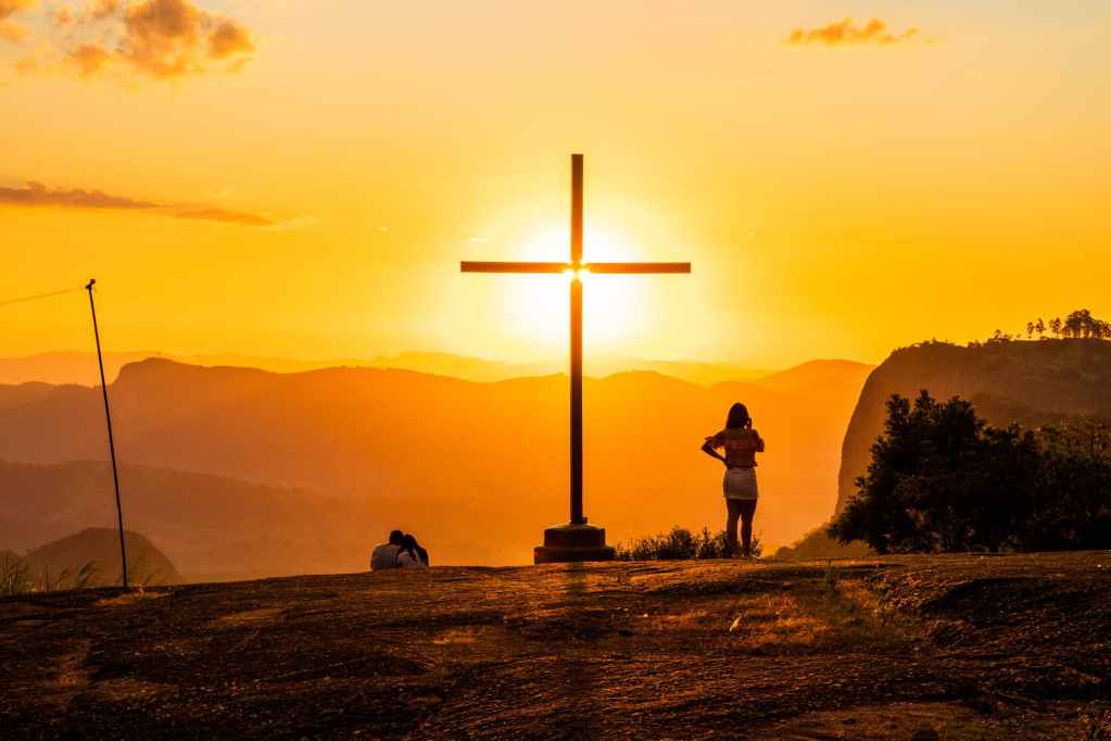 unrecognizable tourists near cross illuminated by bright sunlight at night