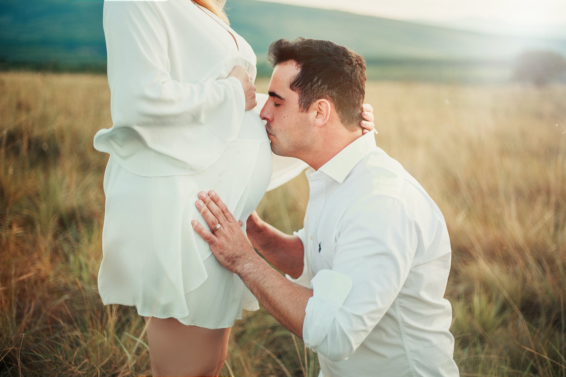 man kissing belly of pregnant woman in green field